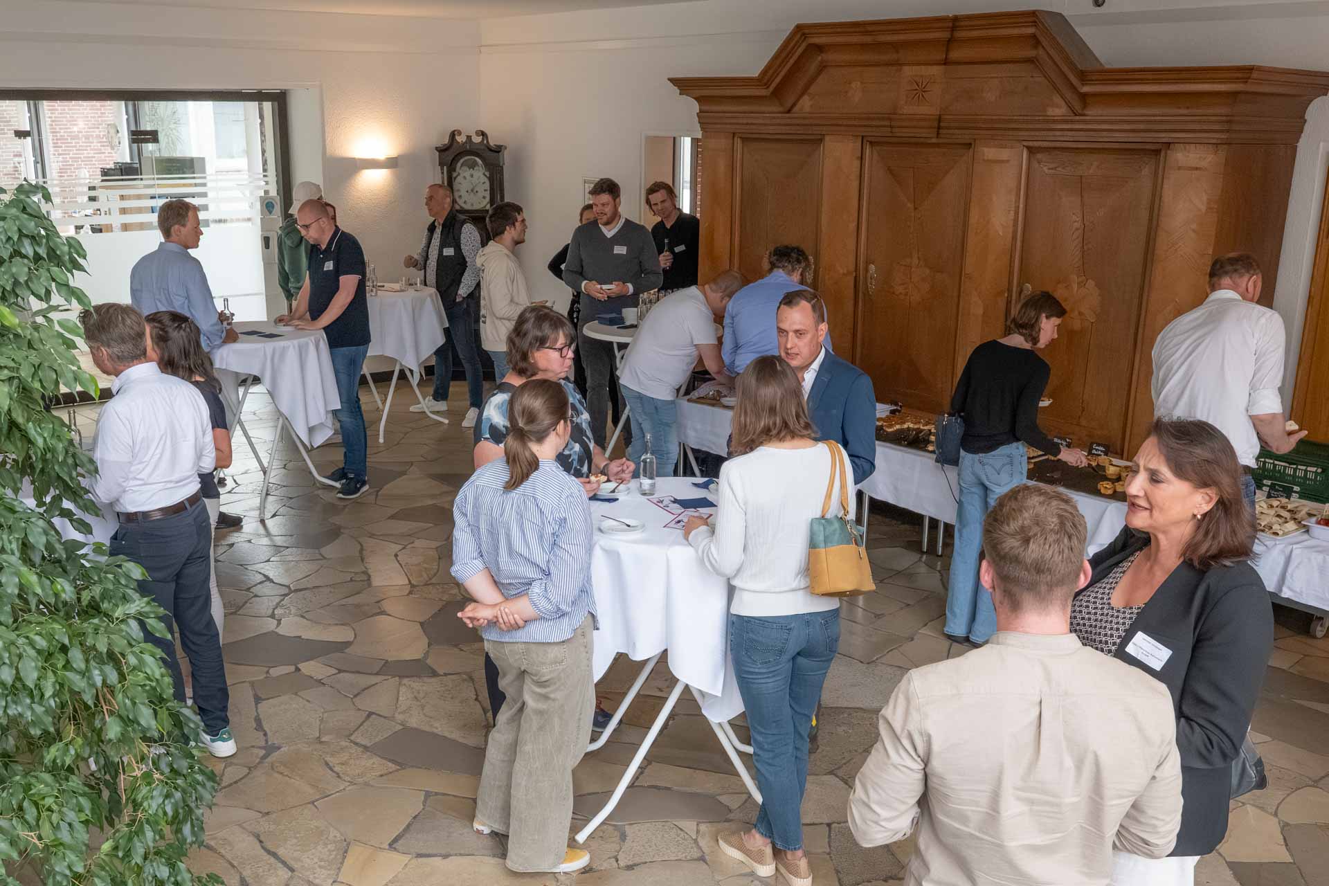 Menschen im Gespräch zwischen Stehtischen und einem Buffet in einer Halle